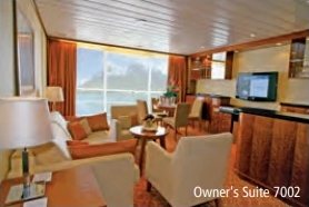 Salon de l’Owner’s Suite 7002 avec canapés, fauteuils et grande baie vitrée.
