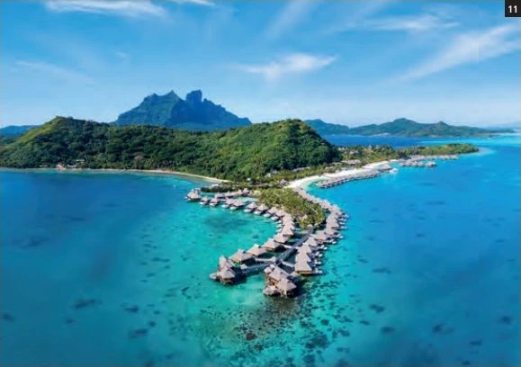 Vue aérienne du Conrad Bora Bora Nui sur l’île de Toopua, avec ses villas sur pilotis et le Mont Otemanu en arrière-plan.