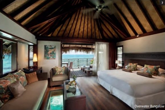 Overwater Bungalow avec salon, plancher vitré et vue sur le lagon depuis la terrasse.