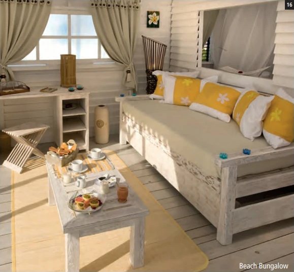 Intérieur clair d'un Beach Bungalow avec lit de repos aux coussins jaunes et table basse dressée pour le petit-déjeuner.
