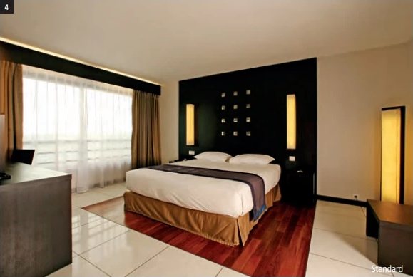 Chambre Standard de l'Hotel Tahiti Nui avec lit double, tête de lit sombre et grande baie vitrée voilée.