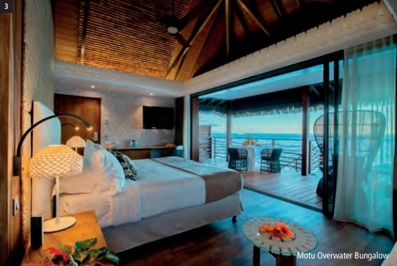 Intérieur d'un Motu Overwater Bungalow de l'InterContinental Tahiti Resort & Spa avec lit, toit en bois et terrasse ouverte sur le lagon.