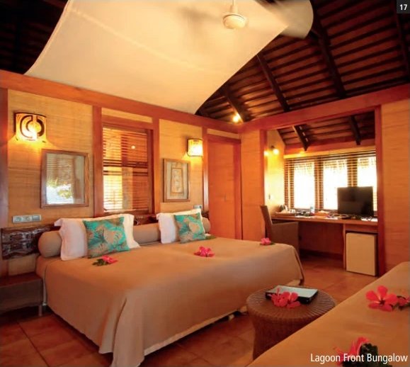 Chambre d'un Lagoon Front Bungalow avec grand lit décoré de fleurs d'hibiscus, plafond en bois et coin bureau.