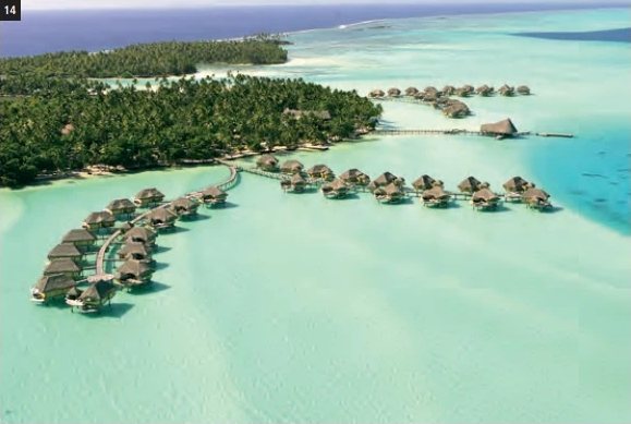 Vue aérienne du Taha'a by Pearl Resorts avec ses bungalows sur pilotis dans un lagon turquoise bordé de cocotiers.