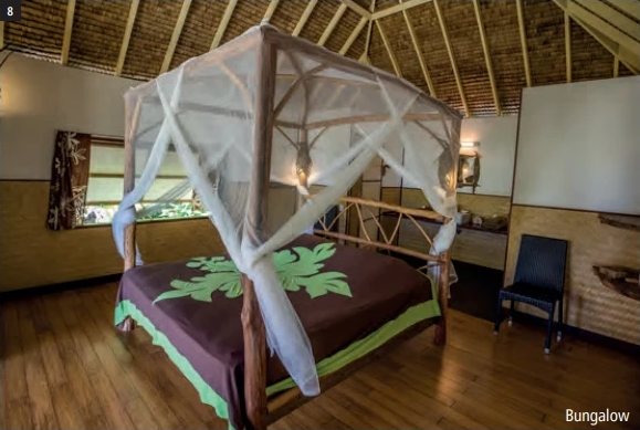 Intérieur d'un bungalow avec lit à baldaquin et moustiquaire, toit en pandanus et parquet en bois.