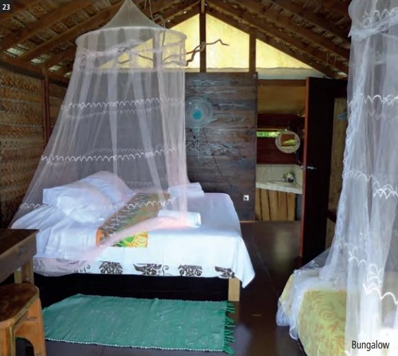 Intérieur d'un bungalow de la Pension Vaiama Village avec lit sous moustiquaire et toit en bois tressé.