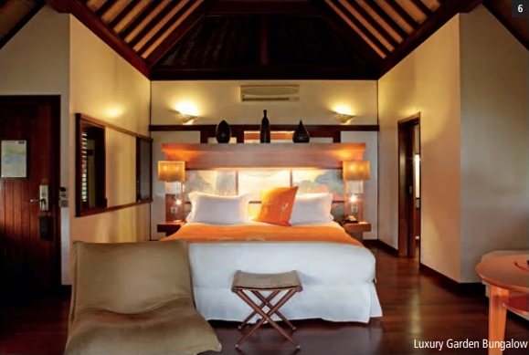 Chambre d'un Luxury Garden Bungalow avec grand lit blanc, coussin orange et plafond en bois sombre.