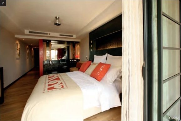 Chambre Studio du Te Moana Tahiti Resort avec grand lit, coussins orange et cuisinette au fond.