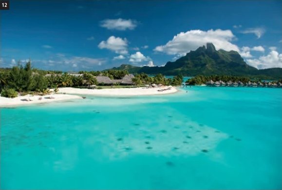 Vue aérienne du St. Regis Bora Bora Resort avec son lagon turquoise, sa plage de sable blanc et le Mont Otemanu en arrière-plan.