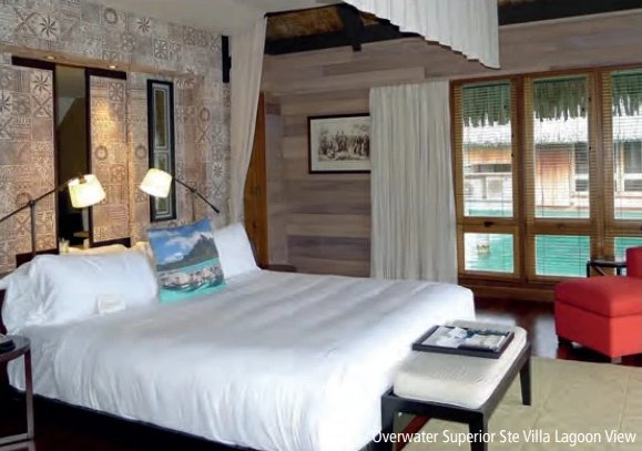Chambre d'une villa sur pilotis du St. Regis avec grand lit blanc et baies vitrées donnant sur le lagon.