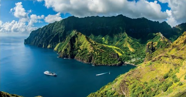 Baie profonde bordée de montagnes verdoyantes et escarpées, avec un navire et un bateau rapide sur la mer bleue.