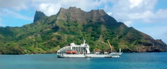 Navire cargo de croisière blanc ancré devant une île montagneuse et verdoyante.