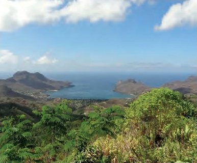 Vue depuis des hauteurs couvertes de végétation tropicale sur une baie entourée de montagnes aux îles Marquises.